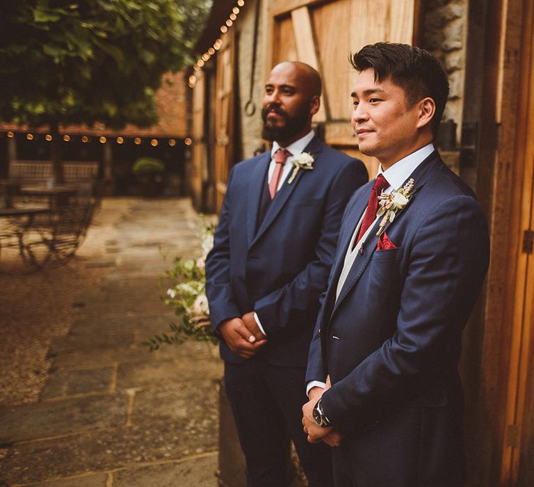 Groom stands with best man in matching blue suits as they wait for the bride at Tythe Barn venue