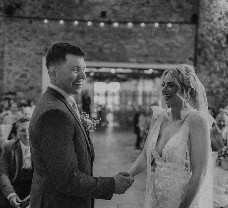 Bride in Made With Love wedding dress holding hands with groom as they both smile at the altar 