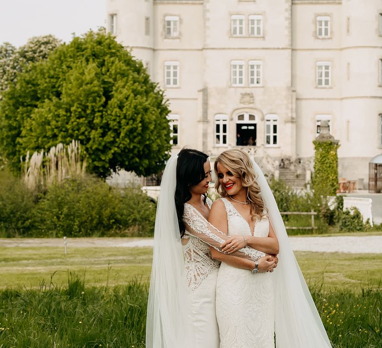 Bride in long sleeve illusion lace wedding dress hugs bride in v-neck lace wedding dress form behind in front of the chateau 