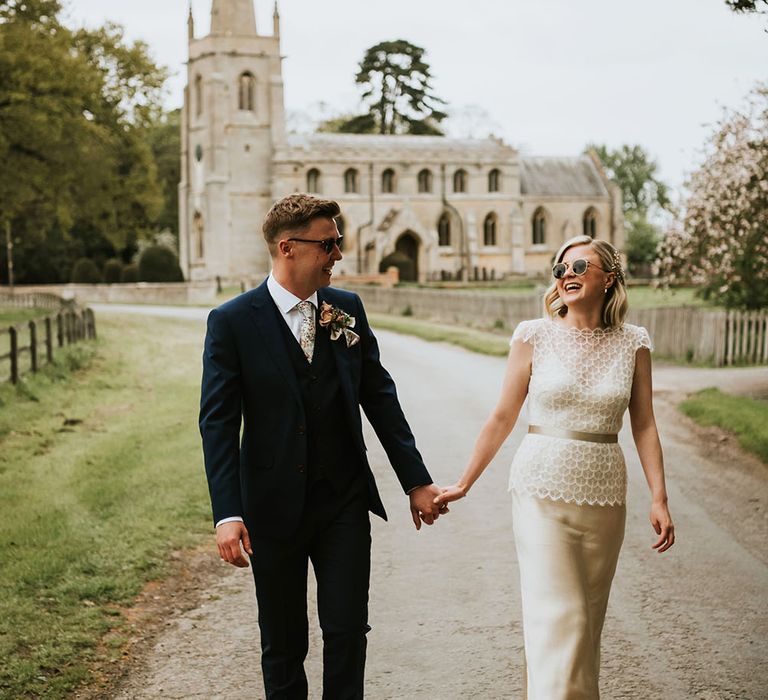 Bride & groom wear sunglasses as they walk hand in hand outdoors at Aswarby Rectory wedding venue 