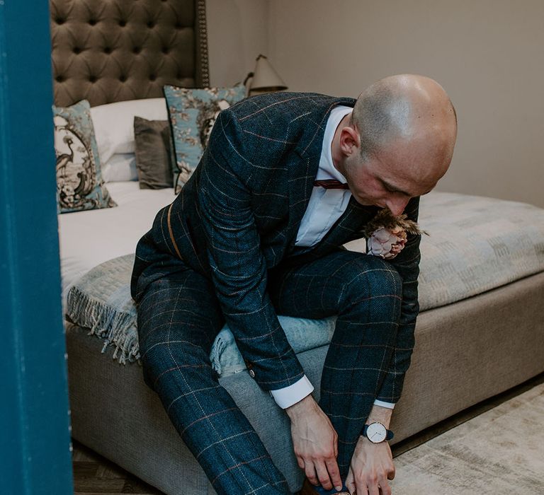 Groom wears homemade buttonhole whilst wearing tartan blazer and trousers complete with red bow tie 