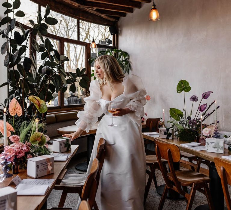 Bride in a JESUS PEIRO wedding dress with voluminous sleeves looking at the wedding reception table favours 