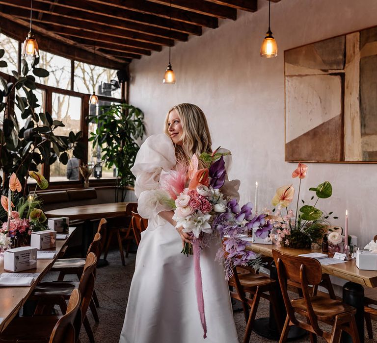 Bride in a JESUS PEIRO wedding dress with voluminous sleeves holding a pastel pink, lilac and white wedding bouquet with orchids, anthuriums and astilbe 