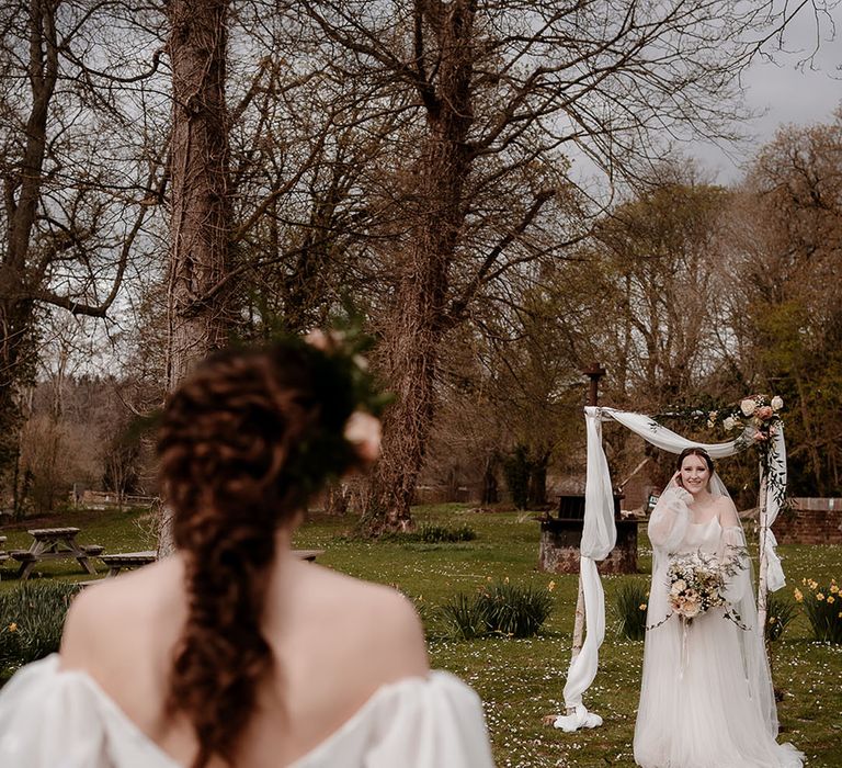 Outdoor wedding ceremony at Mapledurham with bride in an ethereal wedding dress waiting at the altar with drapes and foliage decor 