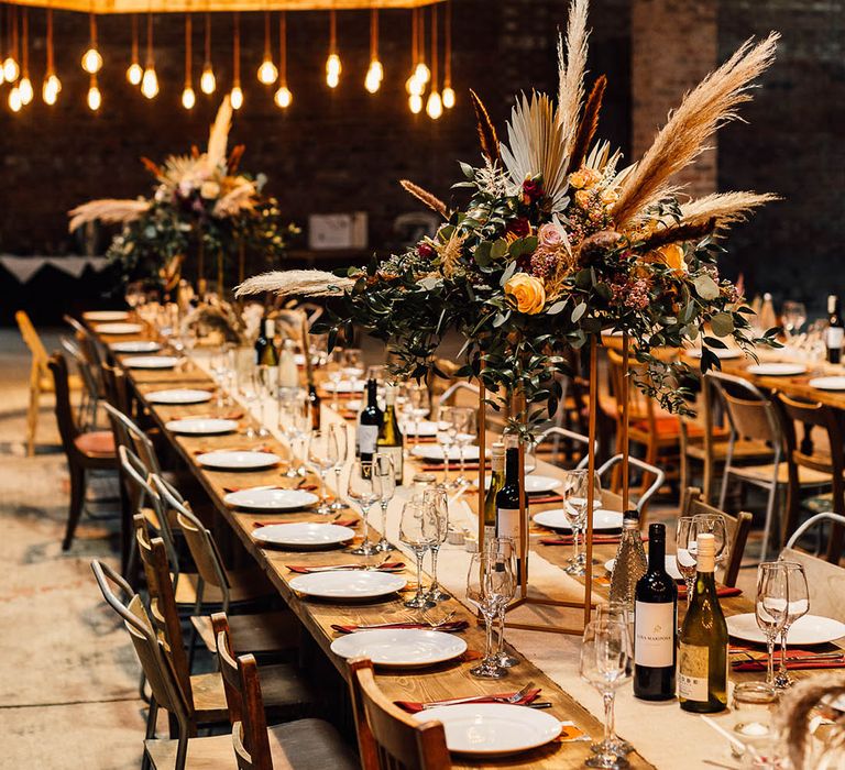 Tall flower table centrepieces with red flowers and dried grasses with low festoon lighting 