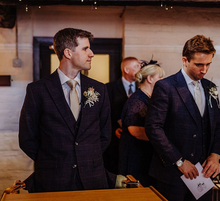 Groom wears a checkered su8it jacket and gold tie with a gold and white buttonhole for hotel wedding 