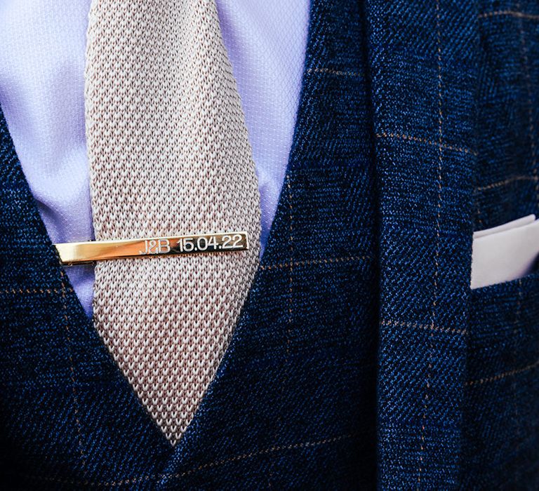 Groom wearing a blue checkered wedding suit with pale tie and personalised gold tie clip 