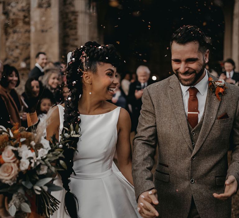 Bride in Sassi Holford wedding dress walks through colourful confetti with her groom in tartan suit complete with Autumnal coloured tie and pocket square