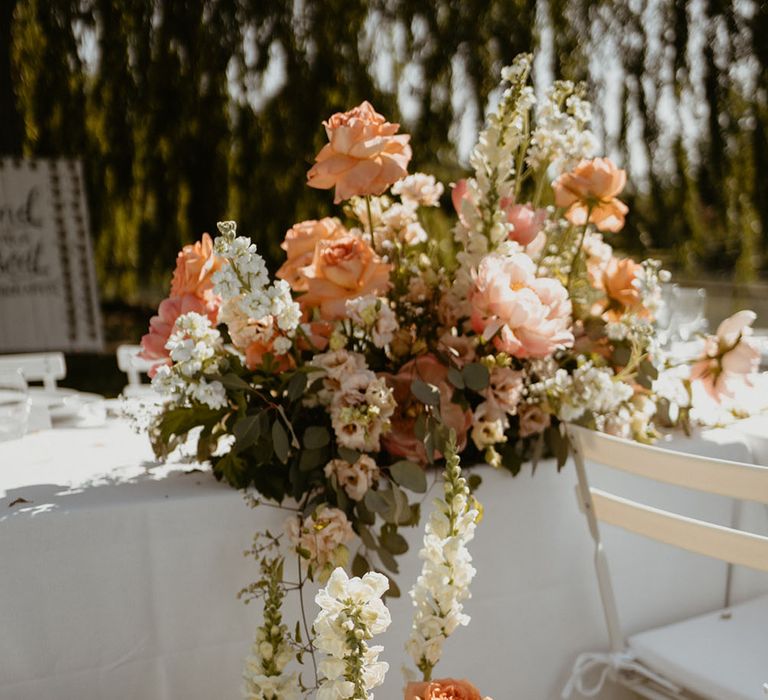 Peach & coral peonies in large floral arrangement outdoors finished with roses and green foliage 