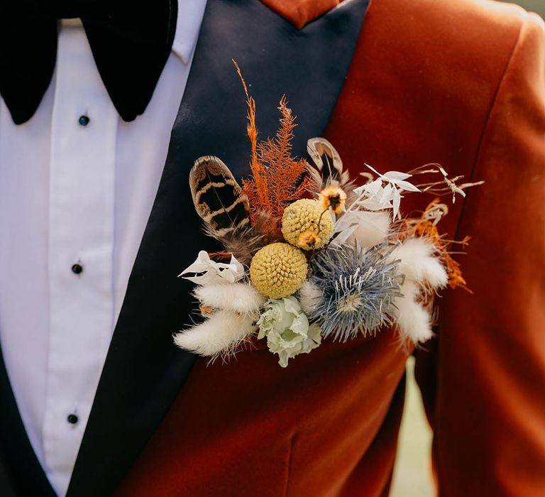 Groom in orange tux wearing a large dried flower buttonhole 