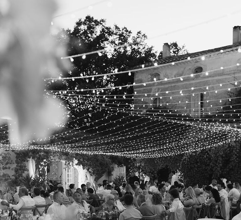 Lit fairy light canopy hangs above wedding guests during outdoor wedding reception in the South of France