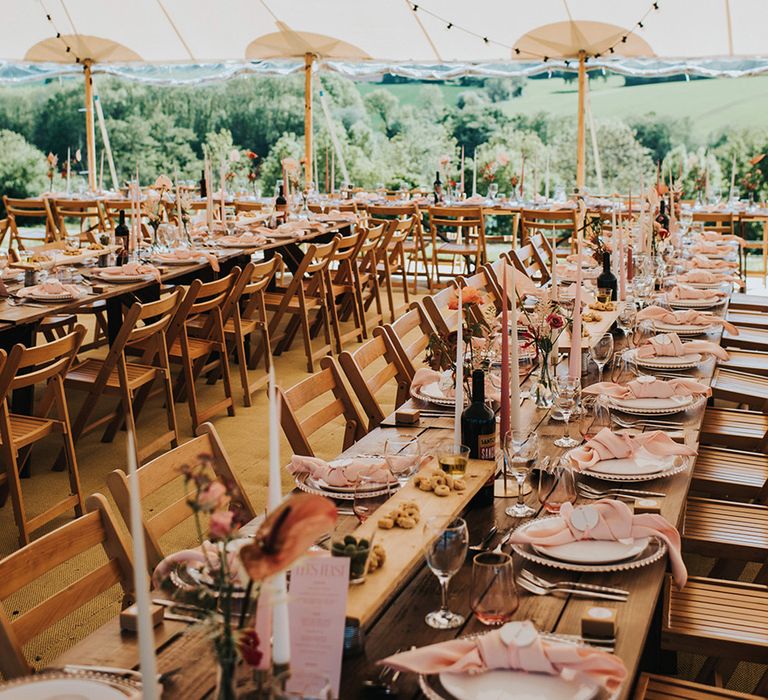 Dark and light pink and white taper candles with pink napkins for the banquet tables with festoon lighting for their marquee wedding 