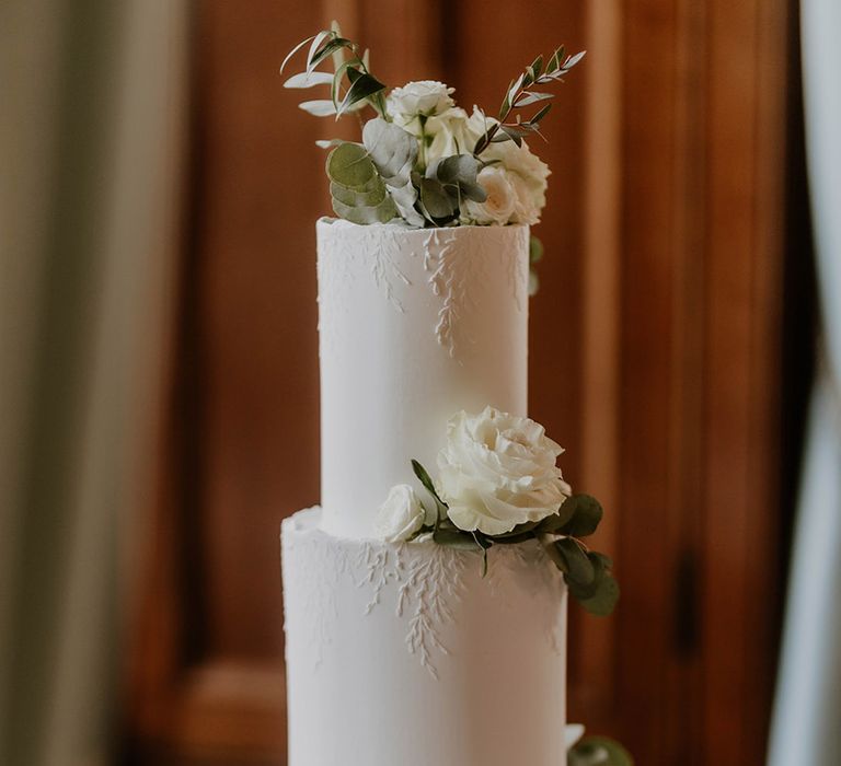 Three tier white wedding cake with textured detail with white roses and foliage 