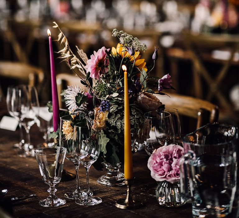 Dark pink and mustard yellow taper candles with pretty colourful flower arrangements for the table decor 