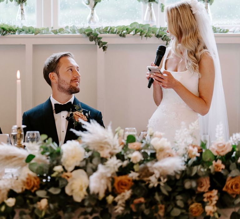 Bride stands up and delivers her bride speech as the groom looks up and listens to her 