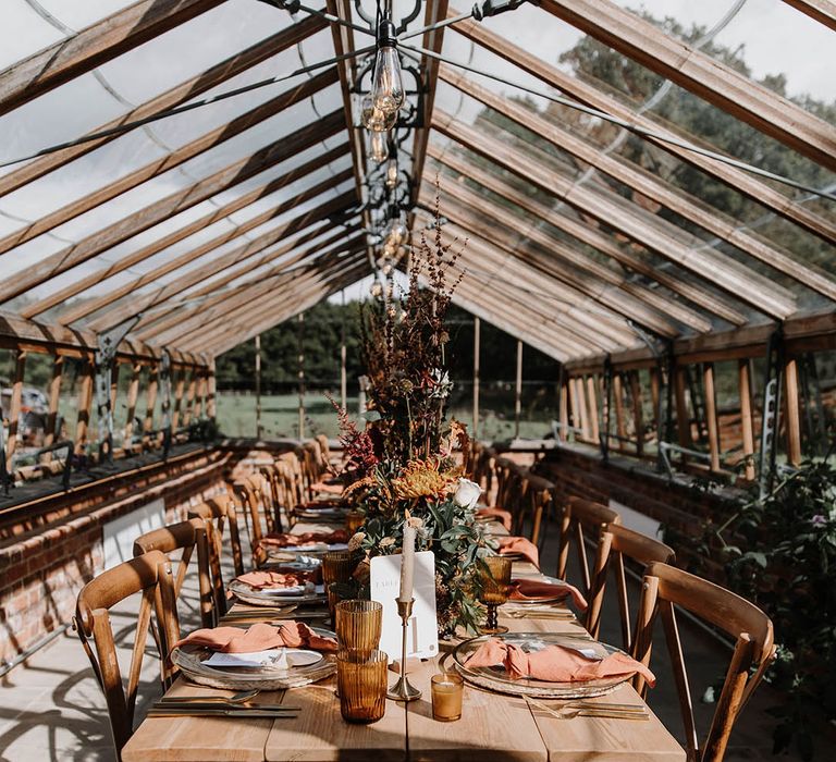 Festoon lighting glasshouse wedding venue with warm toned autumnal decor and flowers