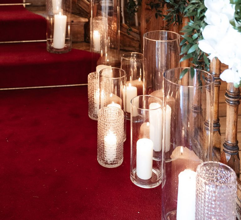 Clear glass cases complete with white pillar candles line staircase finished with white roses and green foliage 