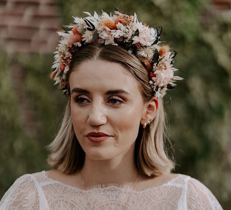 Bride in a sheer lace wedding dress with gold necklace and earrings and a dried boho flower crown 