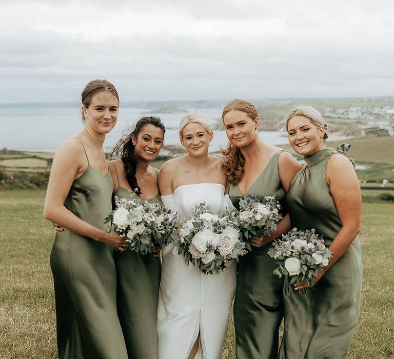 Bride stands with her bridesmaids wearing green satin bridesmaid dresses with differing styles