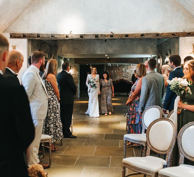 Bride in sparkly wedding dress with shoulder pads walking down the aisle with the mother of the bride 