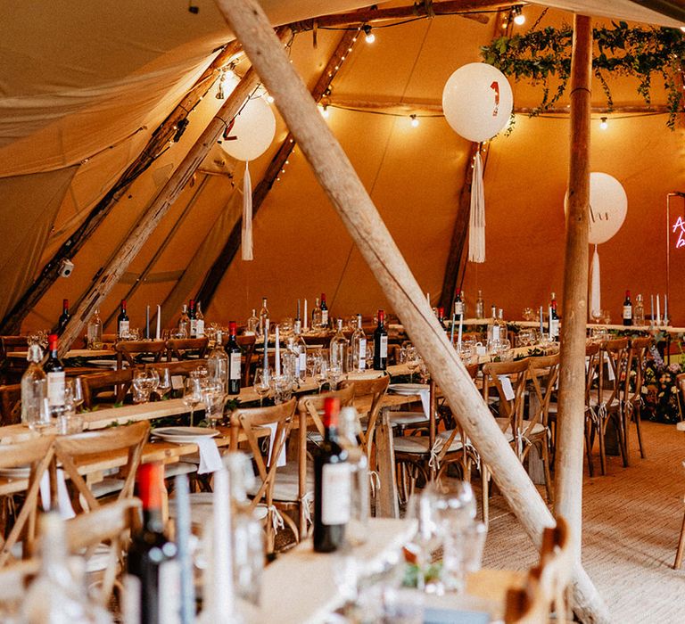 Tipi wedding reception with the pink neon sign and white balloon and tassel wedding table number signs with gin stations 