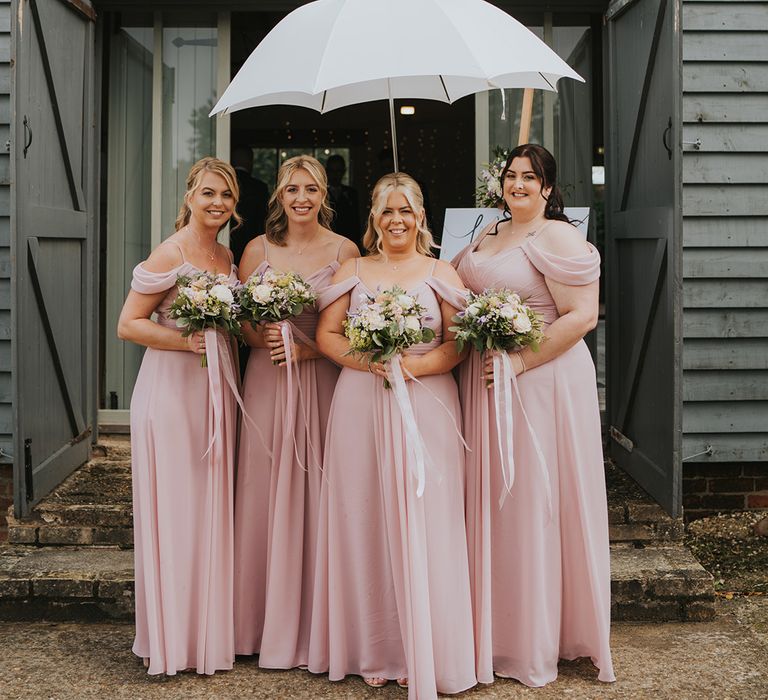 Bridesmaids in matching off the shoulder pink bridesmaid dresses under an umbrella 