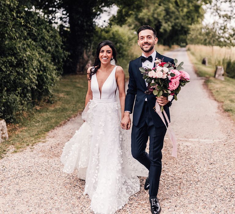 Bride in floral applique Savin London wedding dress walking hand in hand with the groom at botanical and intimate wedding 