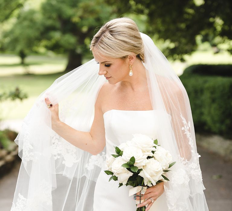 Bride in fitted mermaid wedding dress from Pronovias with embroidered veil holding classic white rose bouquet 