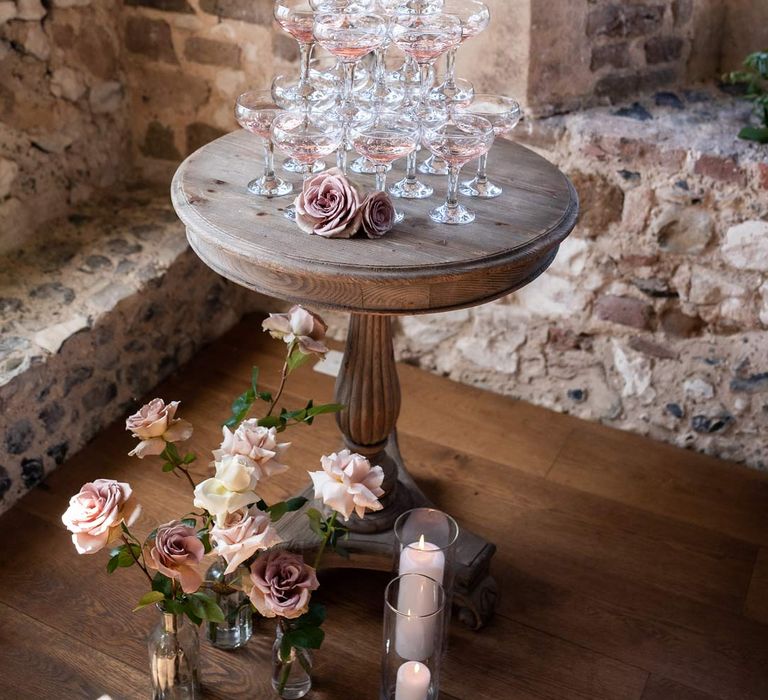 Pink wedding champagne tower on wooden table with garden roses and pillar candle decorations 