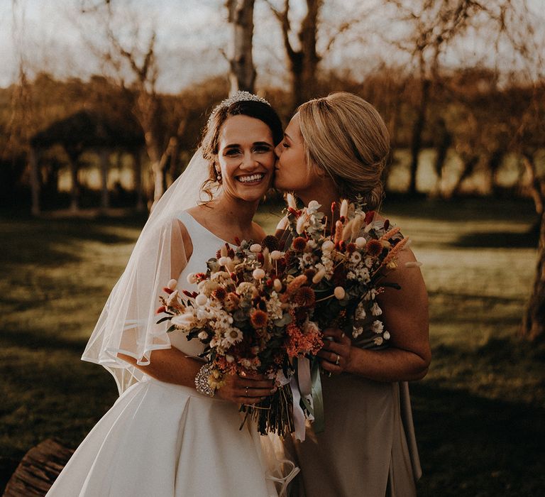 Maid of honour in satin sage green bridesmaid dress smiling with the bride in off the shoulder wedding dress with dried flower wedding bouquets