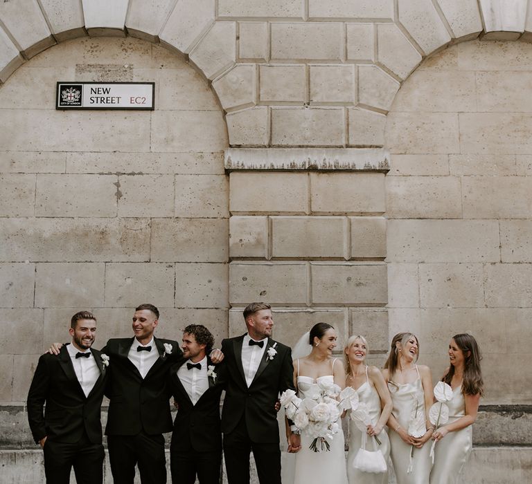 The wedding party group shot with the groom and groomsmen in black tie and the bride and bridesmaids in white wedding outfits 