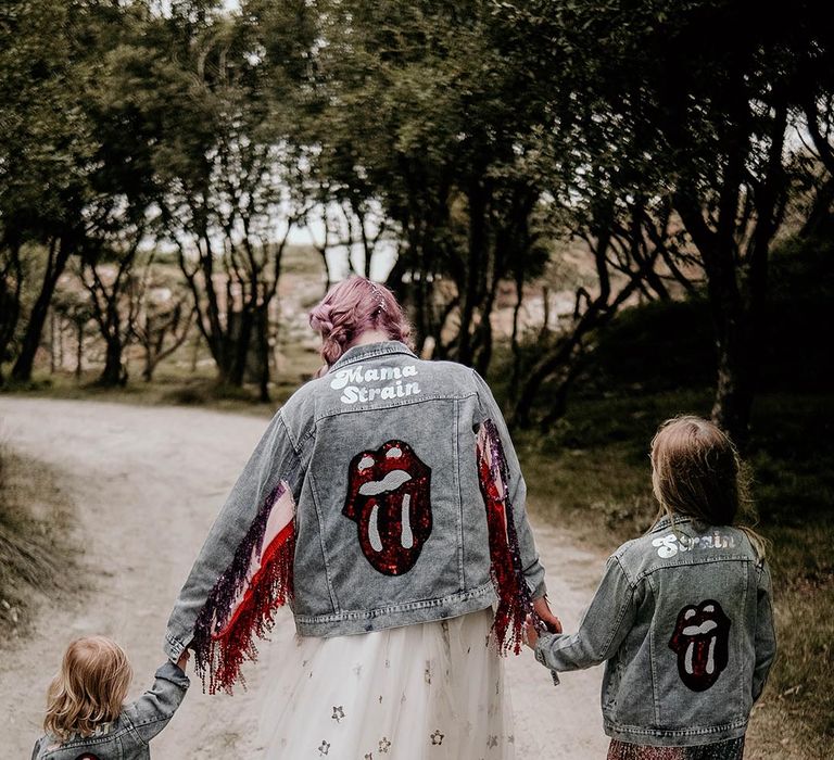 Bride in light blue wash bridal denim jacket with sequin Rolling Stones logo with sparkly tassels matching her two children 