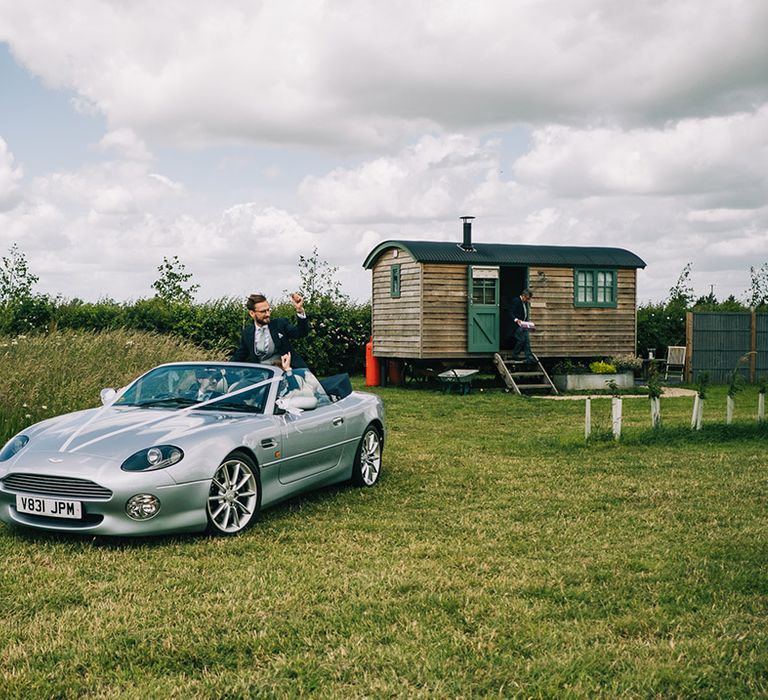 Groom and best man riding in their silver Aston Martin wedding car 