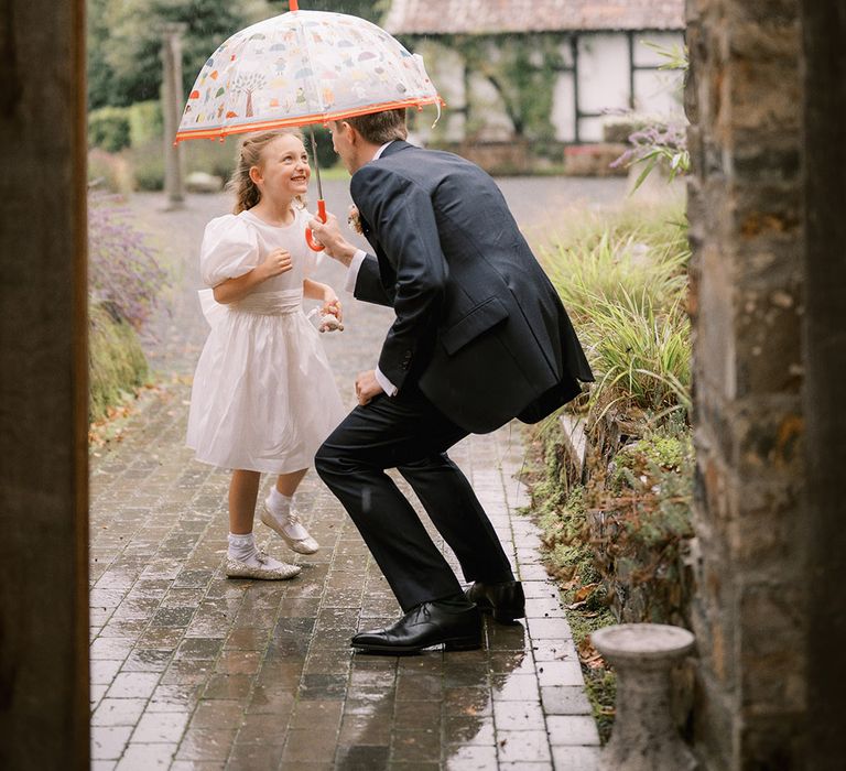 Groom holding an umbrella over the little girl as the rain starts 