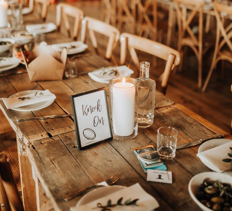 Tall white pillar candle in a hurricane vase with a small photo frame with the table name on 