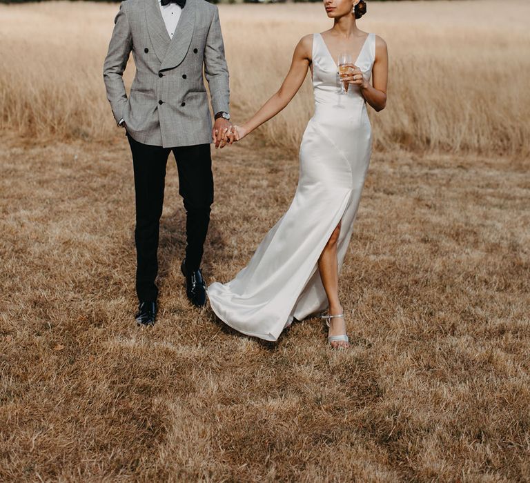 Bride in plunging satin wedding dress with groom in double breasted grey jacket with black buttons 