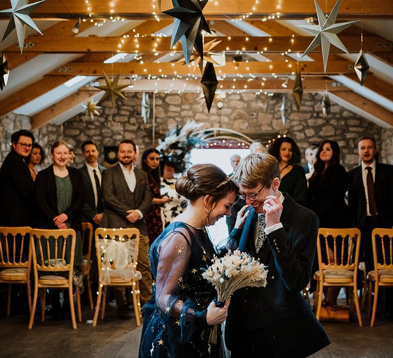 Bride in a navy blue wedding dress laughs with the groom as they walk back down the aisle together as husband and wife 