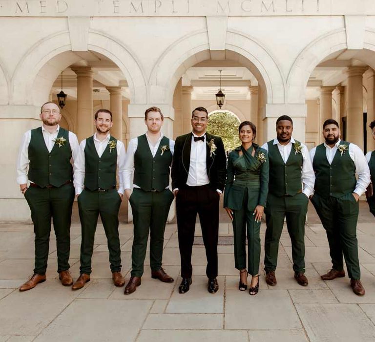 Groom in bottle green velvet grooms suit, black bowtie and chic boutonniere standing with grooms party in bottle green wedding outfits at Inner Temple Hall