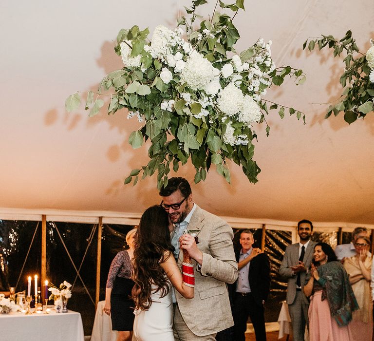 Bride with brown tousled long hair in slip wedding dress dancing with the groom for their first dance at the marquee wedding 