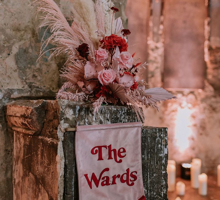 Dyed pink pampas grass in arrangement of preserved wedding flowers above retro style wedding banner sign 