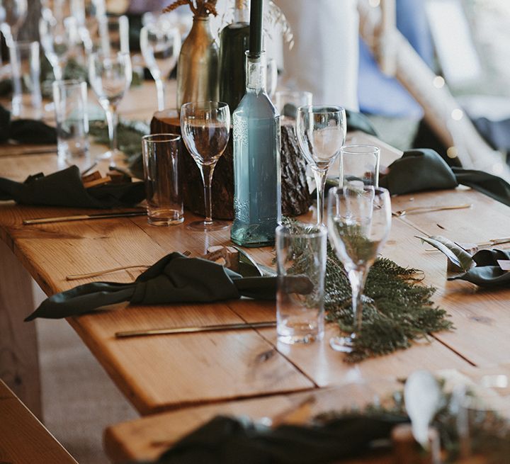 Boho wedding tablescape with dark green napkins, dried flowers, green foliage and glass bottles