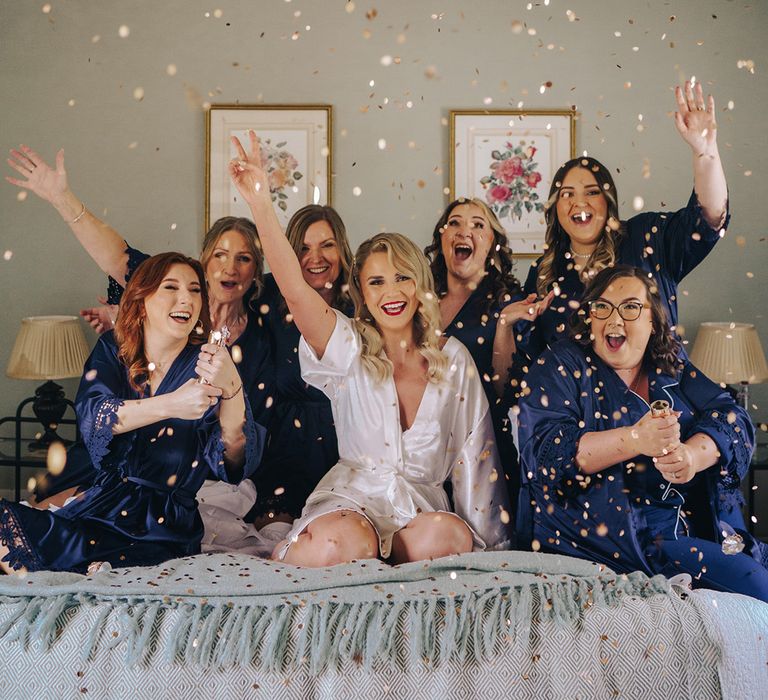 Bridesmaids in satin navy robes and pyjamas popping gold confetti canon as they get ready together 