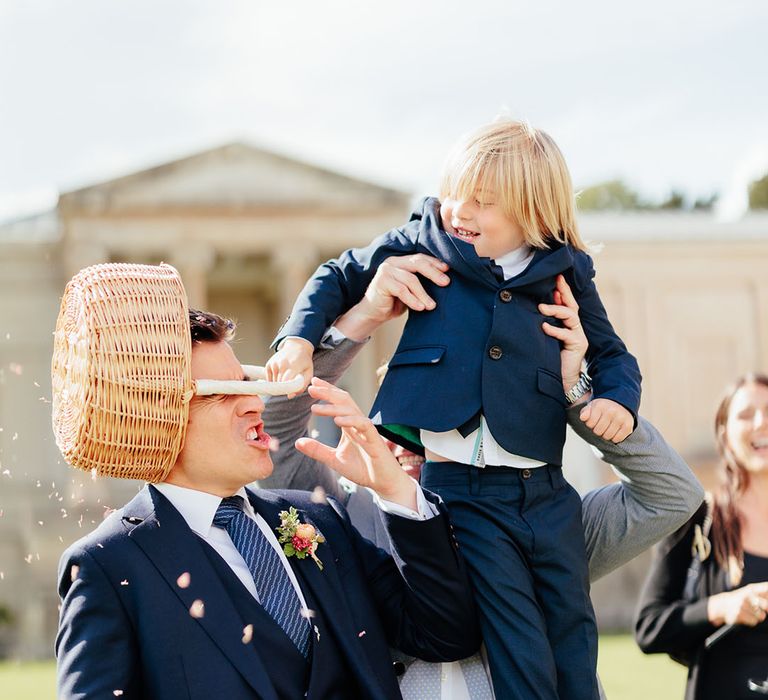 Page boy tips wicker basket full of petal confetti over the groom 