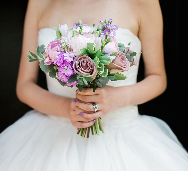 Bride in strapless gown holding bouquet showing off her lilac purple nails for wedding 