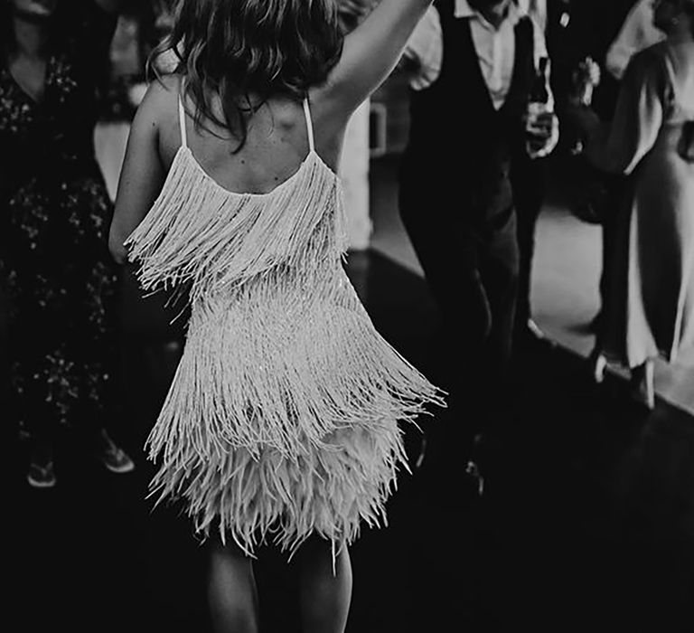 Black and white image of a bride dancing at her wedding reception while wearing a tassle mini dress by Carrie Lavers Photography