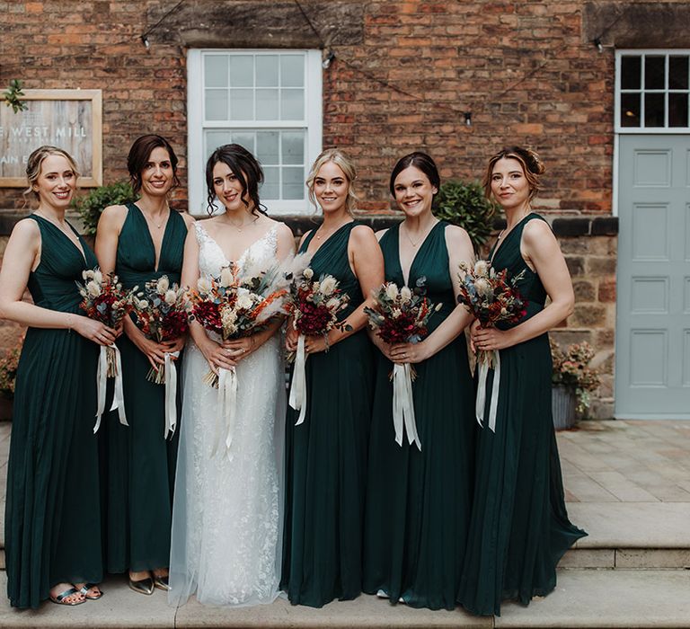 Bridesmaids wearing dark green bridesmaid dresses carrying bouquets tied with white ribbons for autumn wedding 