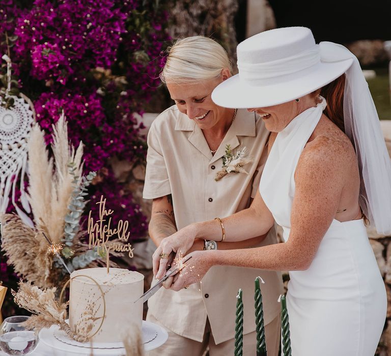 Two brides cut their single tier wedding cake with personalised cake topper 