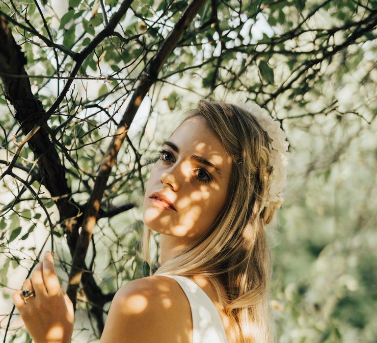 Bride poses outside with nature in a white flower headband and soft wavy hair 