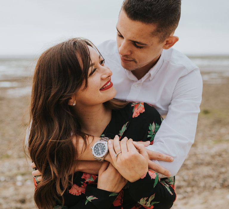 White brunette bride-to-be in a black and red floral dress with red lipstick looking up at her groom-to-be