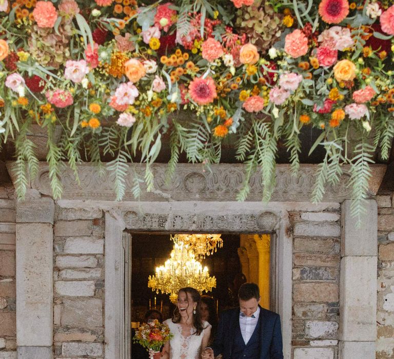 The bride and groom exiting a stone doorway under a display of flowers